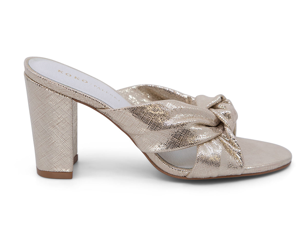 Gold high-heeled shoe with a knotted design on a white background side view